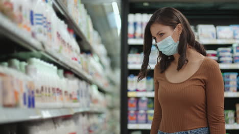 A-girl-goes-to-the-refrigerator-in-a-supermarket-in-a-protective-mask.-Buy-products-in-a-mask